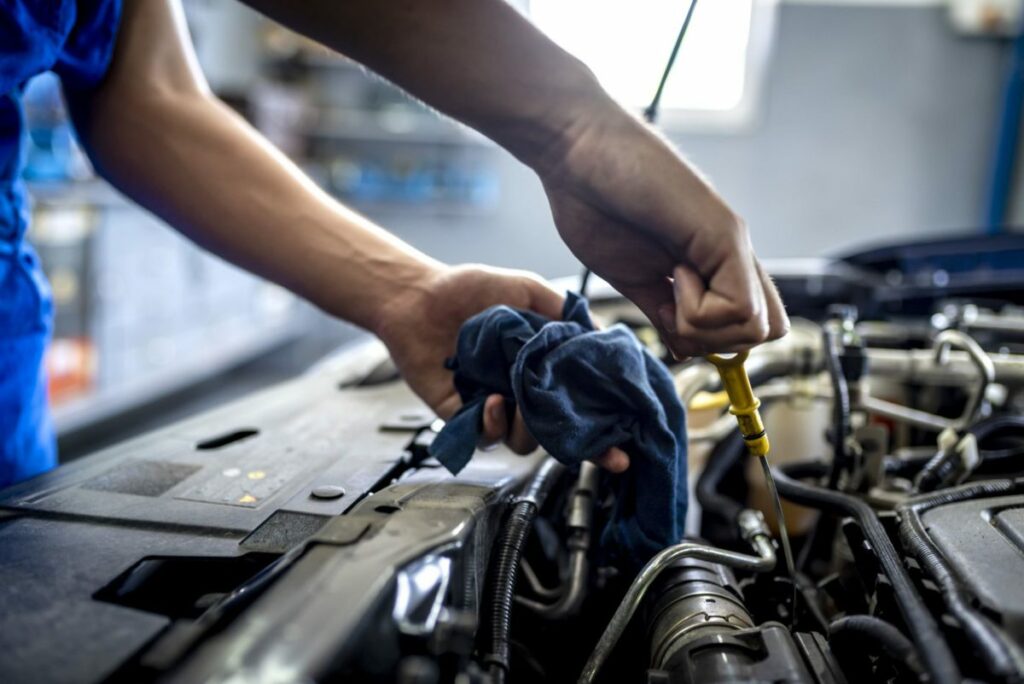 Photo of male mechanic measuring the oil level of an engine at an auto shop. Mechanic checking oil level in a car service garage. Repairing engine at service station. Car repair.