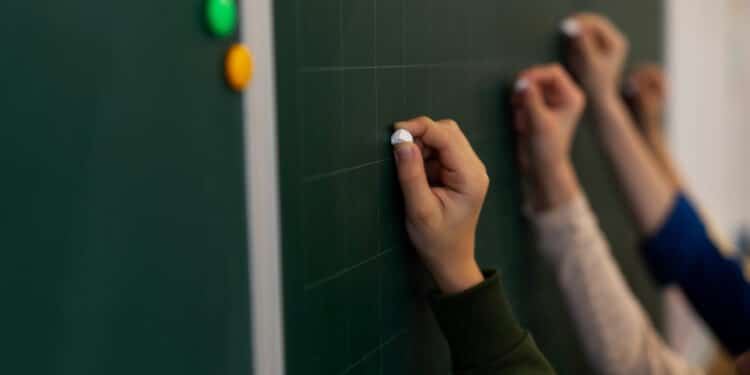 As mГѓВЈos de quatro crianГѓВ§as, cada uma segura um giz em direГѓВ§ГѓВЈo a uma lousa de escola em uma atividade de alfabetizaГѓВ§ГѓВЈo.