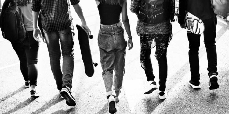 Um grupo de jovens de costas caminhando. A imagem ГѓВ© em preto e branco.