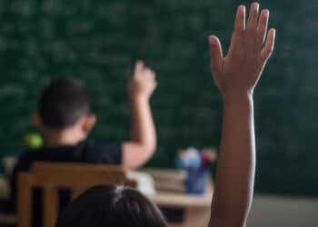 Em primeiro plano vemos uma criança parda levantando a mão em uma sala de aula do ensino médio para pesquisa de disparidade racial