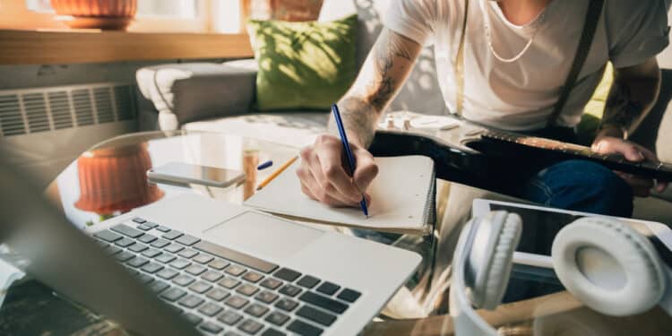 Um homem sentado em frente a um notebook enquanto consulta folhas de anotaГѓВ§ГѓВµes sobre o curso online do MEC, com um lГѓВЎpis na mГѓВЈo