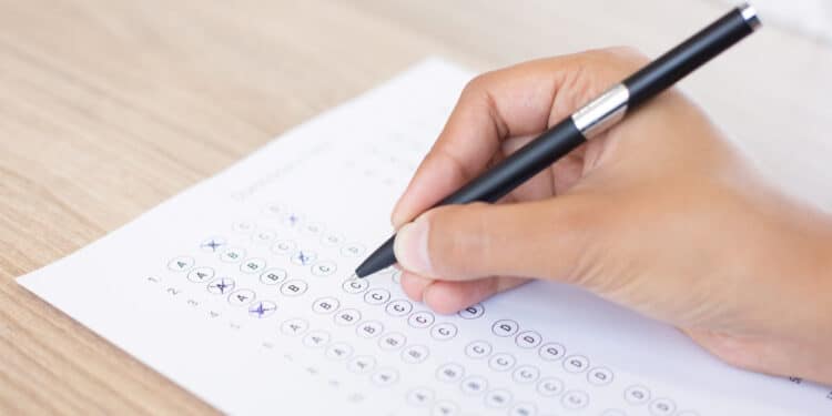 A mГѓВЈo de uma pessoa com saГѓВєde mental segurando um lГѓВЎpis e marcando opГѓВ§ГѓВµes das respostas do vestibular em um papel de teste