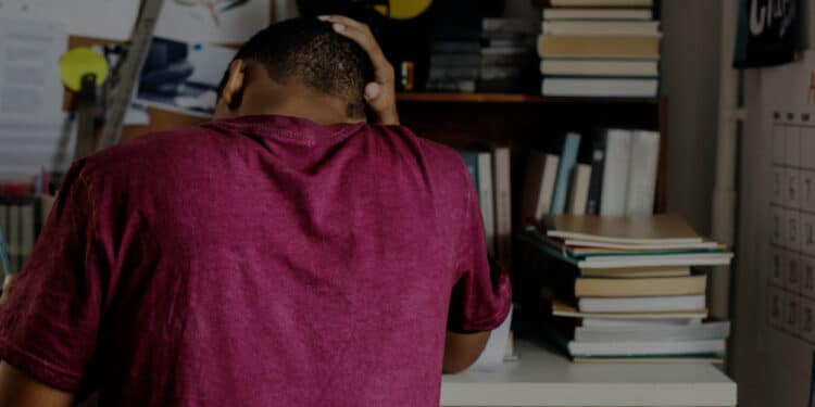 De costas um adolescente com a mГѓВЈo na cabeГѓВ§a enquanto estuda, demonstrando preocupaГѓВ§ГѓВЈo de nГѓВЈo conseguir bolsa de estudo.