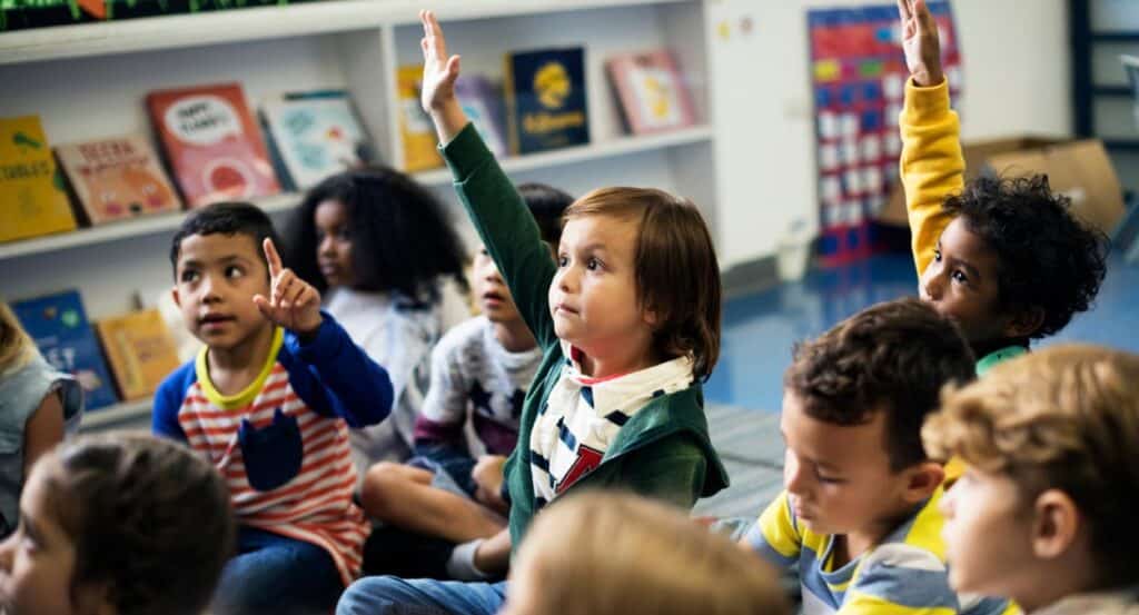 Um grupo de crianças em uma sala de escola primária levantando a mão com educação