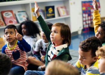 Um grupo de crianças em uma sala de escola primária levantando a mão com educação