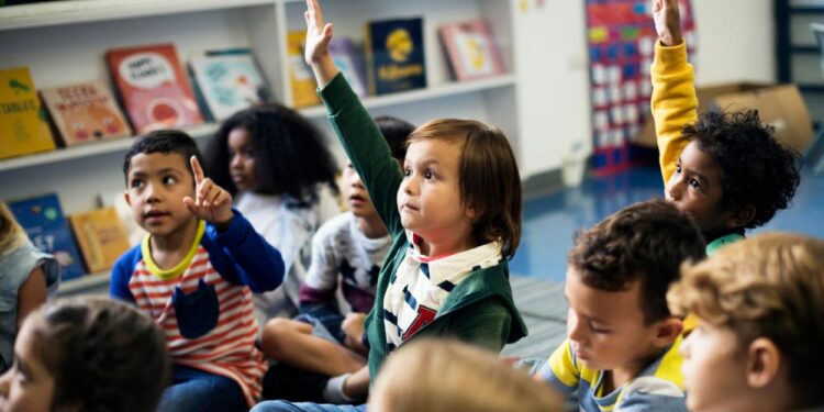 Um grupo de crianГѓВ§as em uma sala de escola primГѓВЎria levantando a mГѓВЈo com educaГѓВ§ГѓВЈo