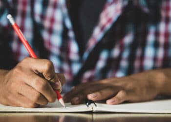 Jovem com uma caneta na mГѓВЈo escrevendo em um caderno