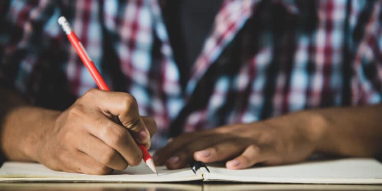 Jovem com uma caneta na mГѓВЈo escrevendo em um caderno