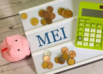 The acronym MEI for Individual Microentrepreneur written on a letter board with a calculator, a piggy bank and Brazilian real coins in the composition. Brazilian economy.
