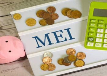The acronym MEI for Individual Microentrepreneur written on a letter board with a calculator, a piggy bank and Brazilian real coins in the composition. Brazilian economy.