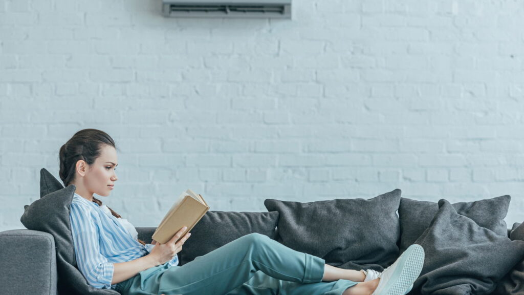 woman reading book on sofa, with air conditioner on wall at home