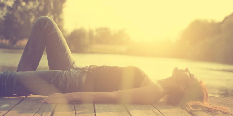 Vintage photo of relaxing young woman on wooden pier at the lake in sunset