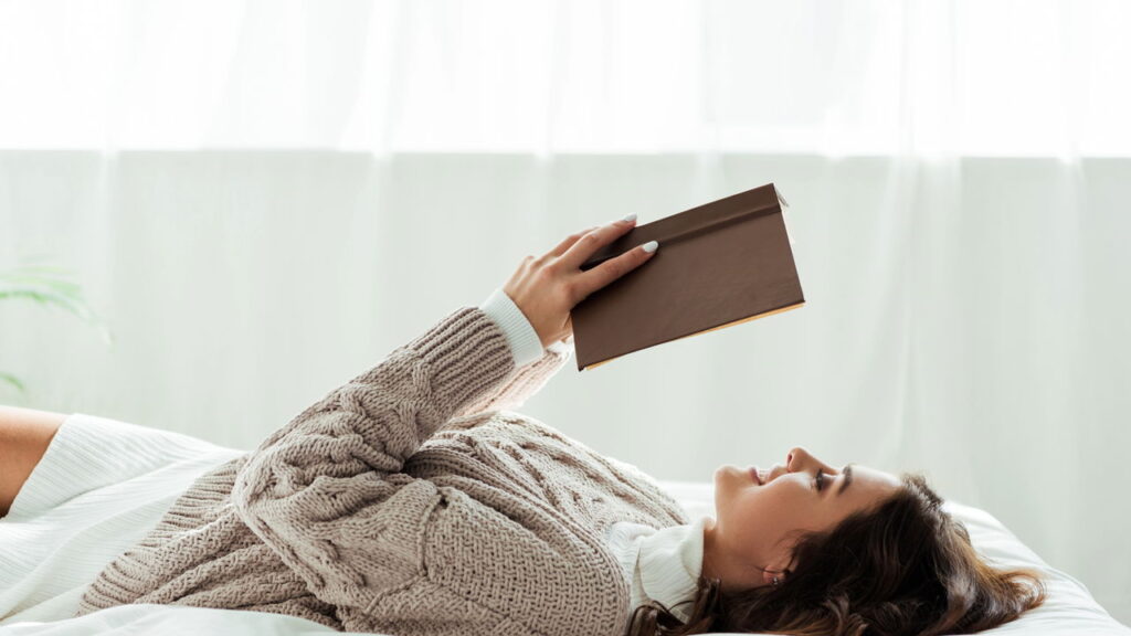 panoramic shot of attractive woman in grey sweater reading book at morning