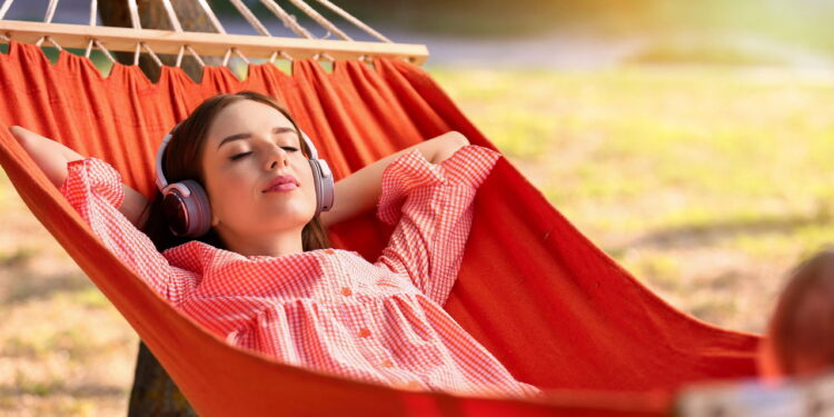 Beautiful young woman with headphones resting in hammock outdoors