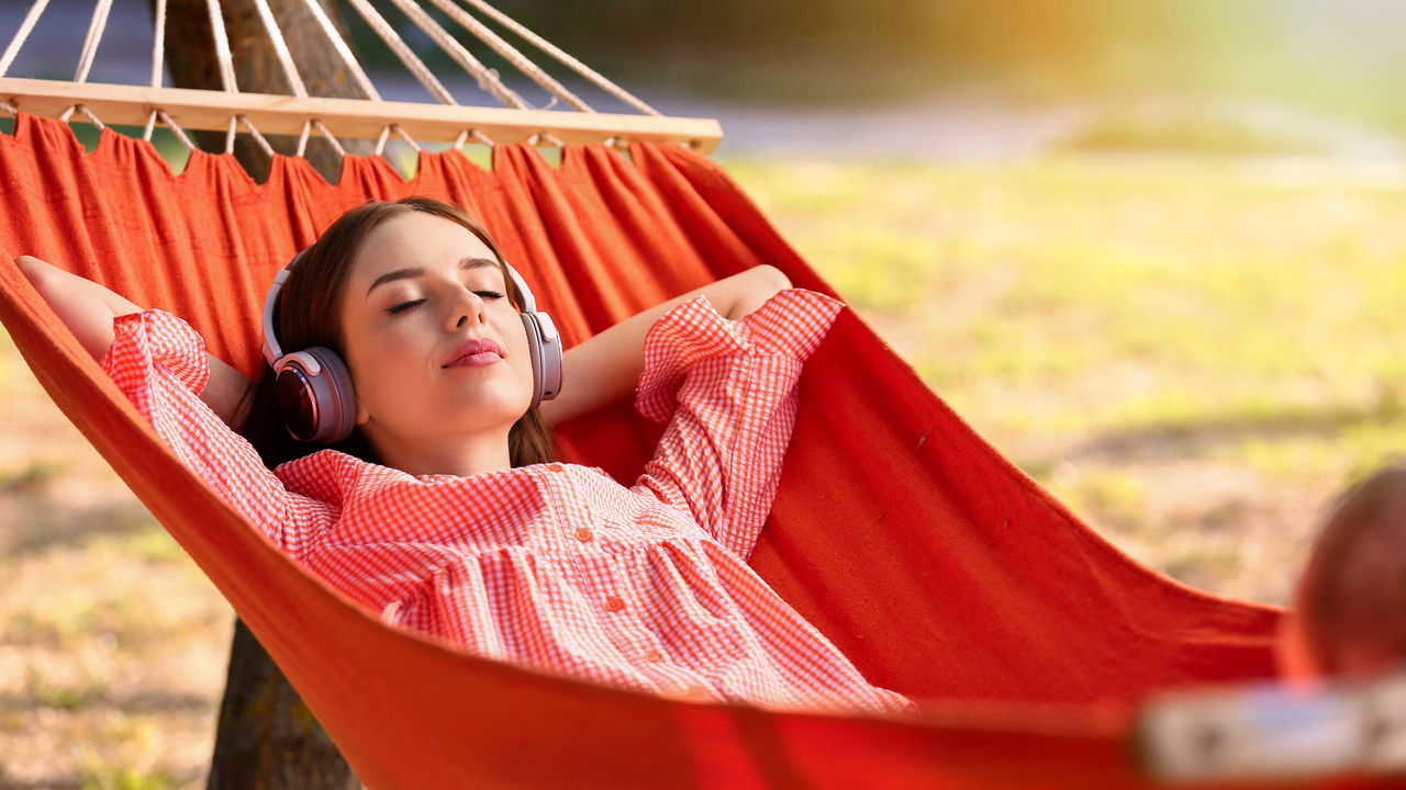 Beautiful young woman with headphones resting in hammock outdoors