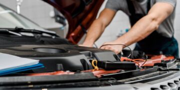Foto recortada de um mecânico com um multímetro verificando a voltagem da bateria de um carro em uma oficina mecânica - Créditos: depositphotos.com / IgorVetushko
