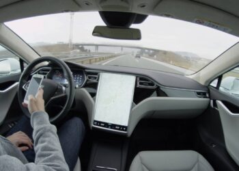 Carro elétrico autônomo Tesla Model S dirigindo sozinho em condições climáticas adversas em uma rodovia, sem intervenção humana. Motorista enviando mensagens de texto em seu dispositivo móvel - Créditos: depositphotos.com / Prostock