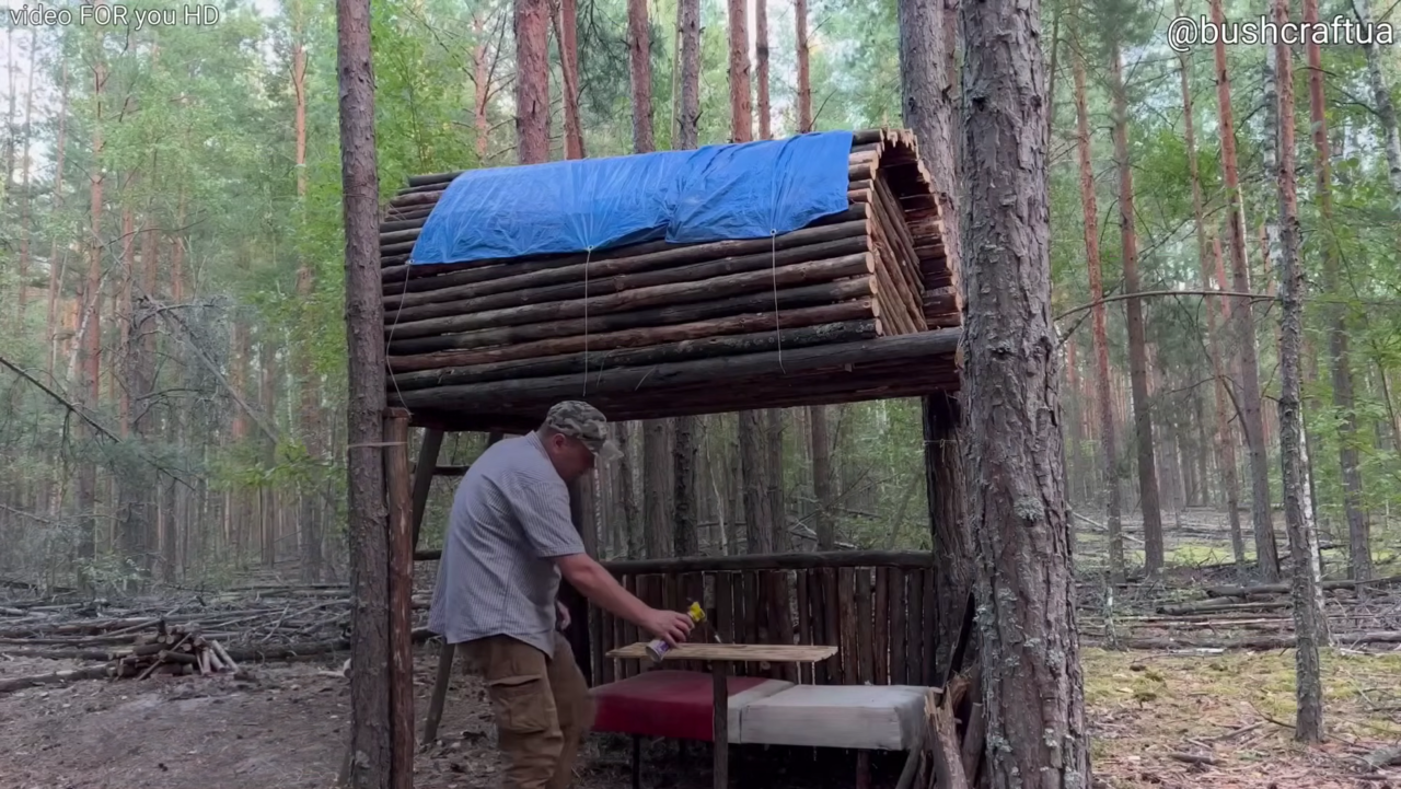 Construtor ergue abrigo elevado entre árvores, suspenso a dois metros do solo, usando apenas troncos e madeira leve