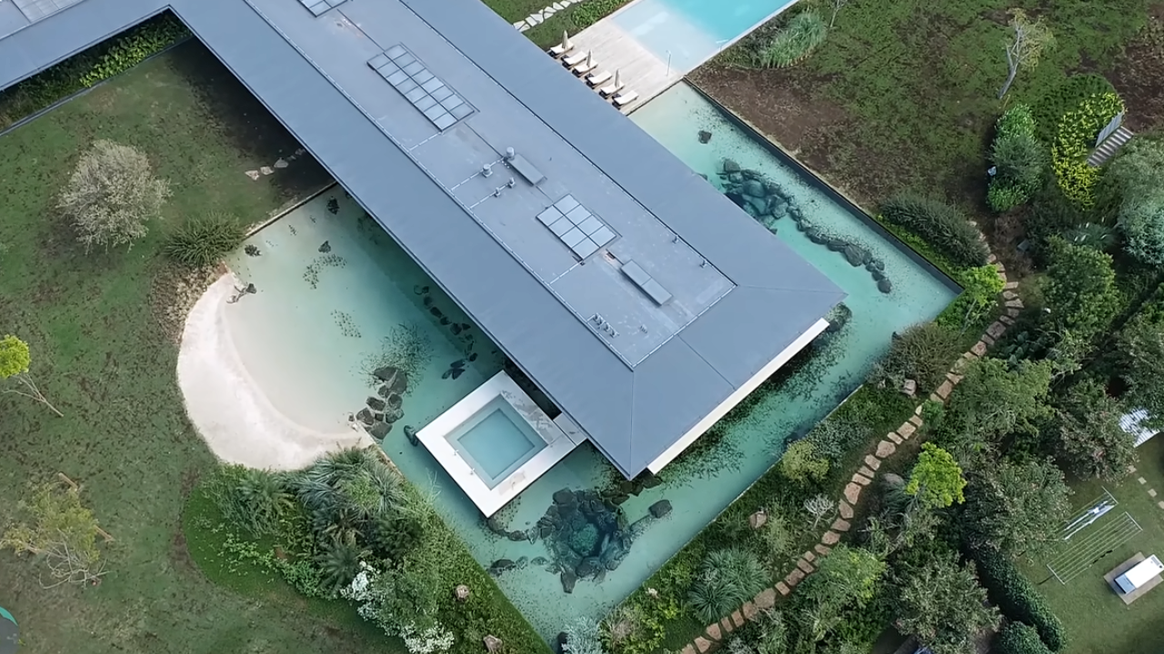 Piscina natural de grande porte envolve a casa e cria um amplo efeito visual de espelho d’água