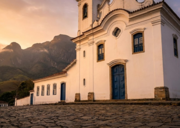 A histórica Matriz de Santo Antônio sob a luz dourada, com as imponentes montanhas da Serra ao fundo.