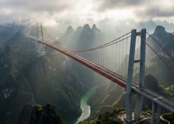 Vista aérea cinematográfica da ponte suspensa sobre o cânion profundo e nebuloso, destacando a altura recorde e as montanhas de Guizhou.