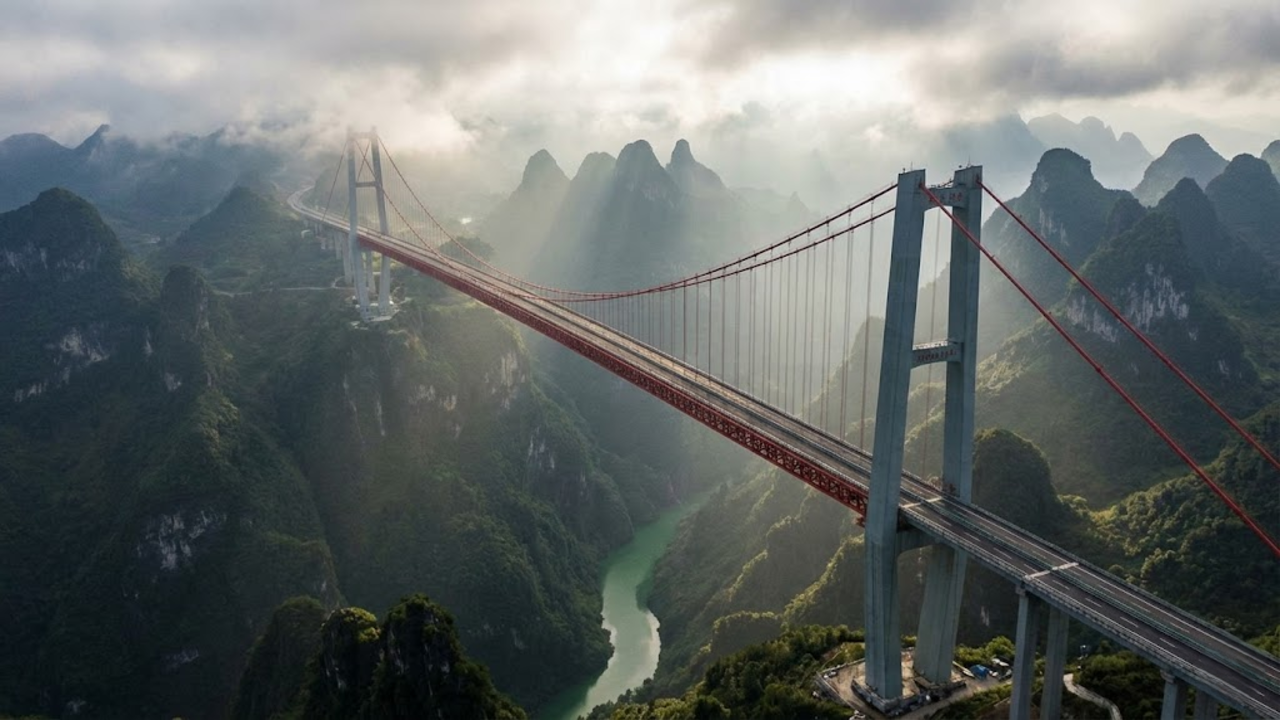 Vista aérea cinematográfica da ponte suspensa sobre o cânion profundo e nebuloso, destacando a altura recorde e as montanhas de Guizhou.