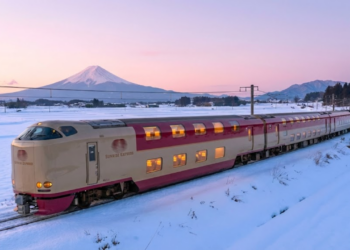 O trem Sunrise Express atravessando uma paisagem de neve ao amanhecer, com o Monte Fuji ao fundo e janelas iluminadas.