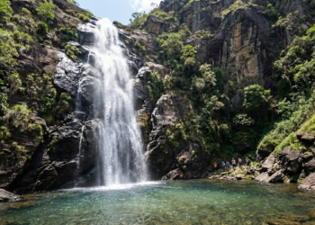 Cachoeira alta cercada por paredões de rocha em um vilarejo pacato no interior de Minas Gerais