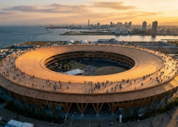 Uma vista aérea impressionante do Great Ring em Osaka durante o pôr do sol, mostrando sua escala gigantesca de madeira abraçando o parque e a baía