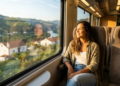 Uma turista sorri maravilhada olhando a bela paisagem portuguesa pela grande janela iluminada do trem