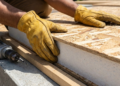 Close-up em primeira pessoa de mãos com luvas encaixando com precisão um painel SIP de madeira e isopor.