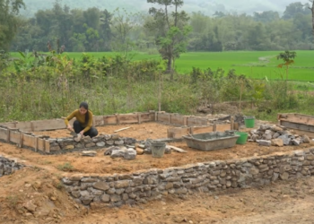 Jovem erguendo paredes de pedra e cimento em projeto de casa autossuficiente e ecológica