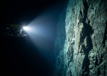 Submarino robô iluminando um paredão rochoso gigantesco no fundo do mar