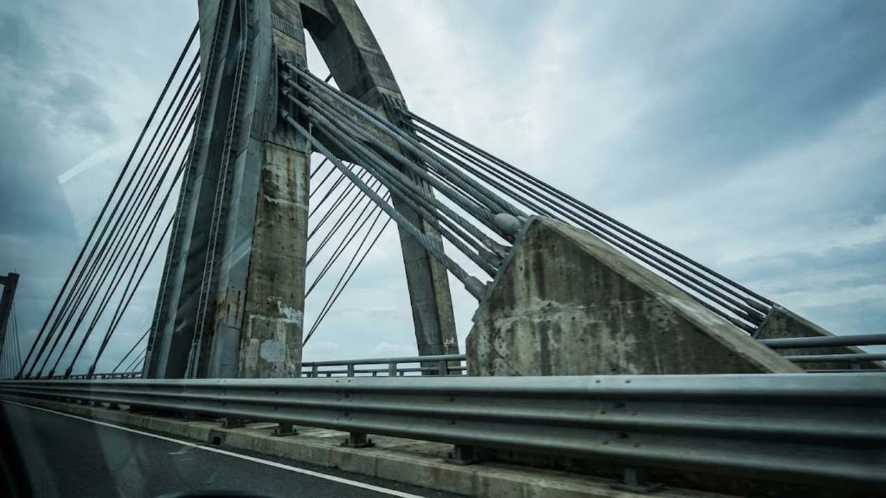 Close em primeira pessoa da estrutura robusta de aço e concreto da ponte sob um céu nublado