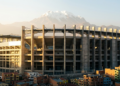 Arena monumental sob a luz dourada com o monte Illimani ao fundo.