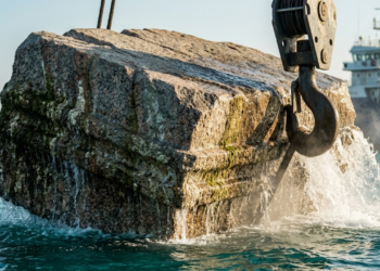 Bloco colossal de granito sendo içado do mar sob a luz do pôr do sol em Alexandria.