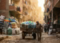 Trabalhador Zabbaleen em rua estreita do Cairo com fardos de plástico sob luz dourada (imagem ilustrativa)