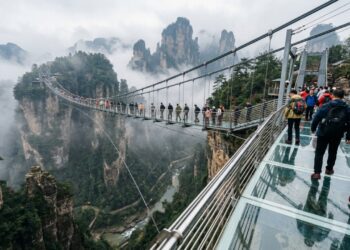Turistas que caminham sobre a ponte transparente a 300 metros de altura sentem as pernas tremerem ao olhar diretamente para o fundo do desfiladeiro rochoso sob seus pés