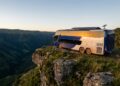 Ônibus Arara Azul estacionado em um penhasco majestoso ao pôr do sol