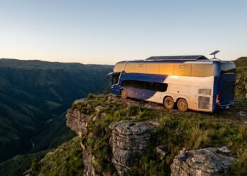 Ônibus Arara Azul estacionado em um penhasco majestoso ao pôr do sol