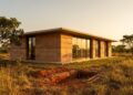 Uma casa moderna e elegante construída com BTC, com texturas táteis sob luz dourada, integrada à paisagem onde o solo foi extraído