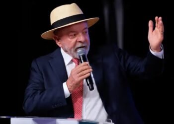 Presidente Luiz Inácio Lula da Silva em primeiro plano, falando no microfone durante discurso em evento.