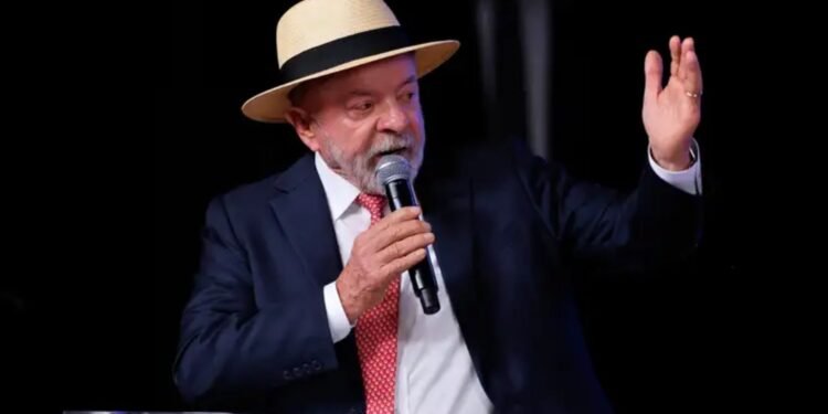 Presidente Luiz Inácio Lula da Silva em primeiro plano, falando no microfone durante discurso em evento.