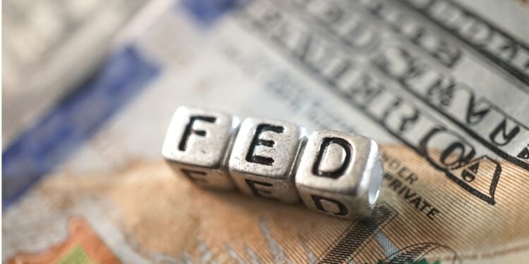 Cubos metálicos formam a palavra “FED” sobre uma nota de dólar americano, em referência ao Federal Reserve e à política monetária dos Estados Unidos.