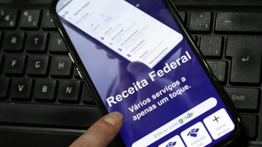 Celular com a página da Receita Federal aberta sobre um teclado de computador.