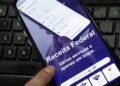 Celular com a página da Receita Federal aberta sobre um teclado de computador.