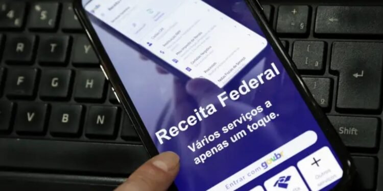 Celular com a página da Receita Federal aberta sobre um teclado de computador.