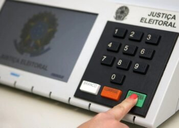Eleitor apertando a tecla "confirmar" na urna eletrônica.