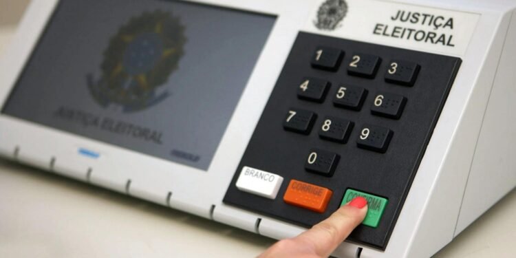 Eleitor apertando a tecla "confirmar" na urna eletrônica.