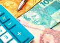 Notas de reais e uma calculadora azul no canto esquerdo da imagem